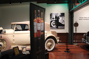 Macallan poster beside a Pre-war/Brass-Era car on display during Bourbon & Brass event.