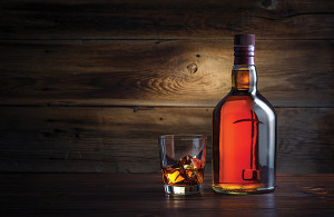 bottle and glass of whiskey with ice on a wooden background